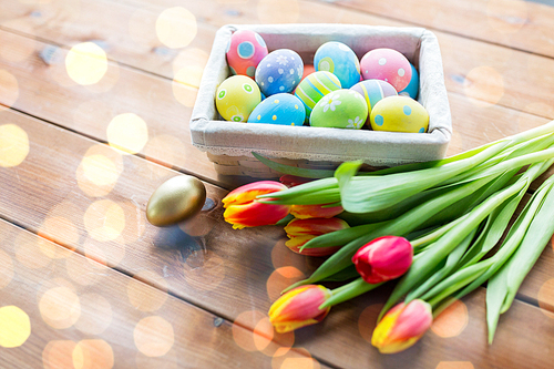 easter, holidays, tradition and object concept - close up of colored easter eggs in basket and tulip flowers