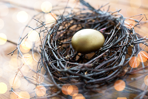 easter, holidays, tradition and object concept - close up of golden easter egg in nest on wooden surface