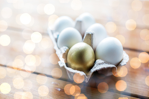 easter, food, cooking and object concept - close up of white and golden eggs in egg box or carton wooden surface