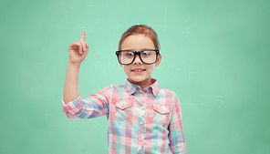 childhood, school, education, vision and people concept - happy little girl in eyeglasses pointing finger up over green school chalk board background