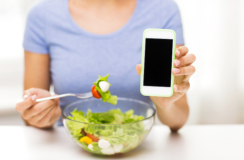 healthy eating, dieting, technology, food and people concept - close up of young woman with smartphone eating vegetable salad at home