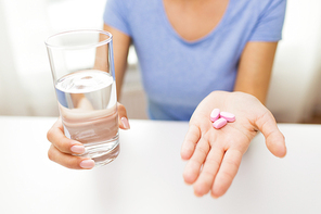 healthy eating, medicine, health care, food supplements and people concept - close up of woman hands holding pills and water glass at home