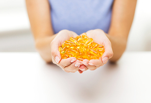 healthy eating, medicine, health care, food supplements and people concept - close up of woman hands holding pills or fish oil capsules at home