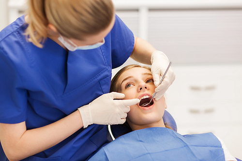 people, medicine, stomatology and health care concept - happy female dentist with mirror checking patient girl teeth up at dental clinic office