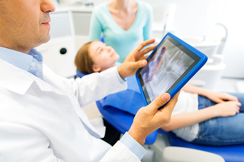 people, medicine, stomatology, technology and health care concept - close up of male dentist with x-ray on tablet pc computer screen and patient girl with her mother at dental clinic office
