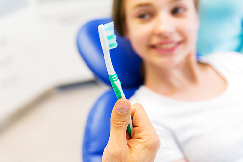 people, medicine, stomatology and health care concept -close up of dentist hand holding toothbrush and patient girl at dental clinic office