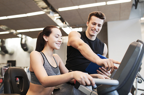 sport, fitness, lifestyle, technology and people concept - happy woman with trainer working out on exercise bike in gym