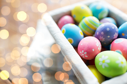 easter, holidays, tradition and object concept - close up of colored easter eggs in basket over holidays lights