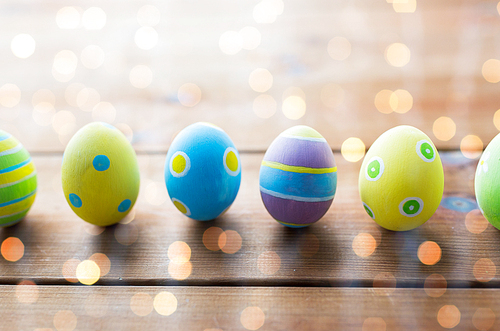 easter, holidays, tradition and object concept - close up of colored easter eggs on wooden surface over holidays lights