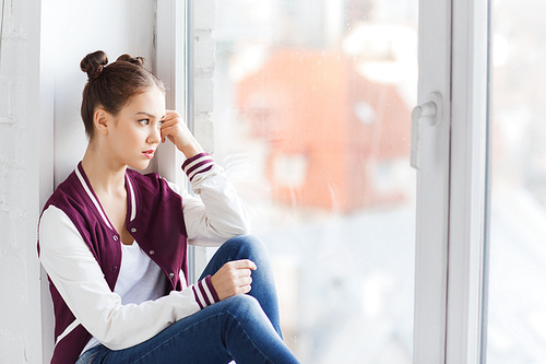 people, emotion and teens concept - sad unhappy pretty teenage girl sitting on windowsill