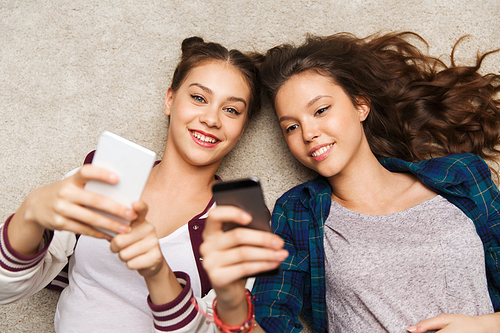 people, friends, teens and friendship concept - happy smiling pretty teenage girls lying on floor with smartphones