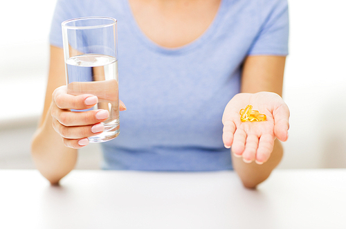 healthy eating, medicine, health care, food supplements and people concept - close up of woman hands holding pills or fish oil capsules and water glass at home