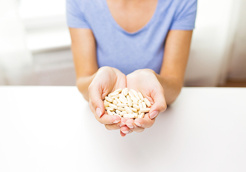 healthy eating, medicine, health care, food supplements and people concept - close up of woman hands with medication or pills at home