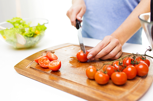 healthy eating, cooking, vegetarian food, dieting and people concept - close up of woman chopping tomatoes with knife on cutting board