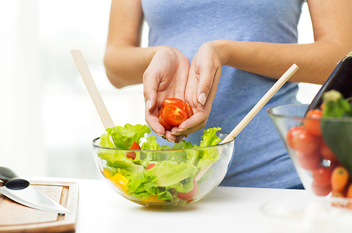 healthy eating, vegetarian food, dieting and people concept - close up of young woman cooking vegetable salad and adding tomatoes at home