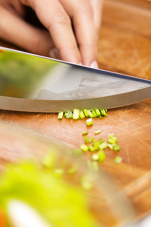 healthy eating, cooking, vegetarian food, kitchenware and people concept - close up of woman chopping green onion with knife on wooden cutting board