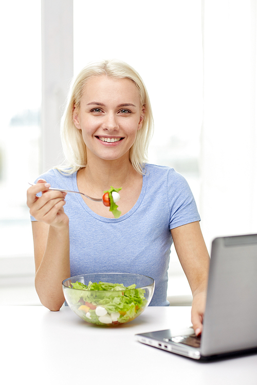 healthy eating, dieting, food, technology and people concept - smiling young woman with laptop computer eating vegetable salad at home