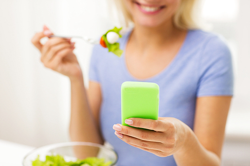 healthy eating, dieting, technology, food and people concept - close up of smiling young woman with smartphone eating vegetable salad at home