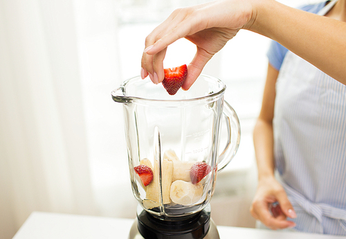 healthy eating, cooking, vegetarian food, diet and people concept - close up of woman with blender making banana strawberry fruit shake at home