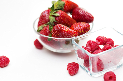 fruits, berries, weight loss,  food and objects concept - close up of juicy fresh ripe red strawberries and raspberries in glass bowls over white