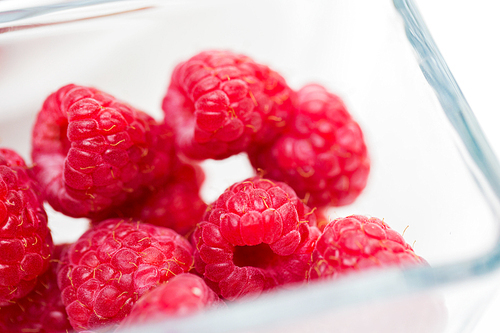 fruits, berries, ,  food and objects concept - close up of ripe red raspberries in glass