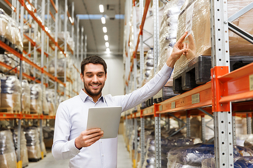 wholesale, logistic, business, export and people concept - happy man or manager with tablet pc computer checking goods at warehouse