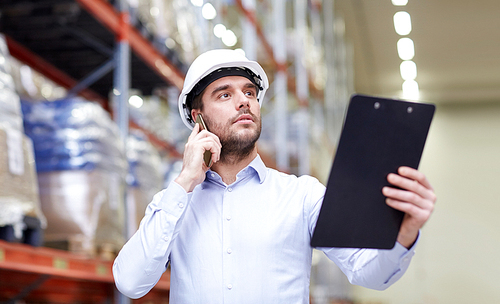 wholesale, logistic, business, export and people concept - businessman with clipboard calling on smartphone at warehouse