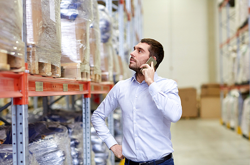 wholesale, logistic, business, export and people concept - serious businessman calling on smartphone at warehouse