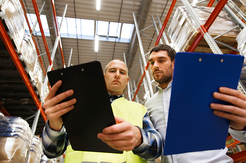 wholesale, logistic, people and export concept - manual worker and businessmen with clipboards at warehouse