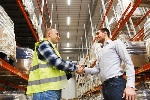 wholesale, logistic, people and export concept - manual worker and businessmen with clipboard shaking hands and making deal at warehouse