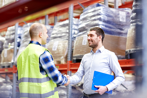 wholesale, logistic, people and export concept - manual worker and businessmen with clipboard shaking hands and making deal at warehouse