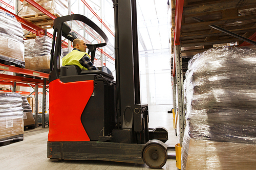 wholesale, logistic, loading, shipment and people concept - man or loader on forklift loading cargo at warehouse