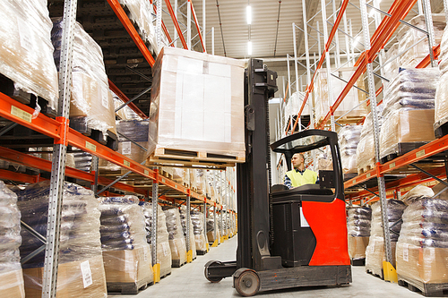 wholesale, logistic, loading, shipment and people concept - man or loader on forklift loading cargo at warehouse