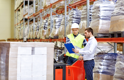 wholesale, logistic, people and export concept - manual worker and businessmen with clipboard at warehouse