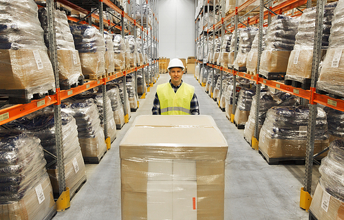 wholesale, logistic, loading, shipment and people concept - smiling man with loader carrying cargo at warehouse