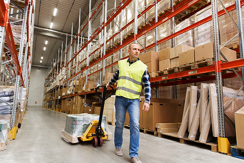 wholesale, logistic, loading, shipment and people concept - man carrying loader with goods at warehouse