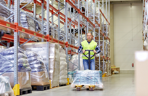 wholesale, logistic, loading, shipment and people concept - man carrying loader with goods at warehouse