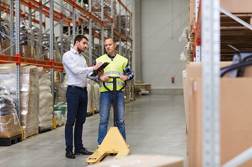 wholesale, logistic, people and export concept - manual worker and businessmen with loader and clipboard at warehouse