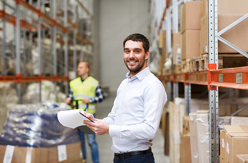 wholesale, logistic, people and export concept - happy businessman or supervisor with clipboards at warehouse