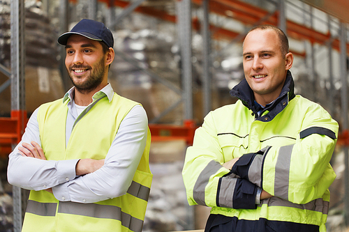 logistic, delivery, shipment, people and export concept - happy men or manual workers in reflective uniform at warehouse