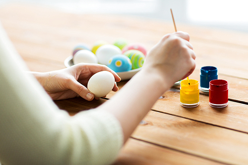 easter, holidays, tradition and people concept - close up of woman coloring easter eggs with colors and brush