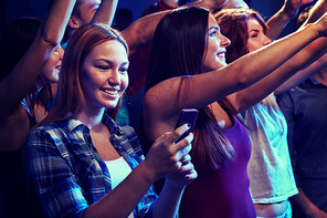 party, holidays, celebration, nightlife and people concept - smiling young woman with smartphone texting message at concert in club