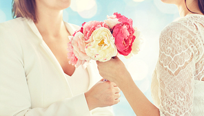 people, homosexuality, same-sex marriage and love concept - close up of happy married lesbian couple with flower bunch over blue holidays lights background