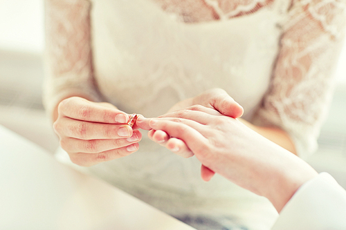 people, homosexuality, same-sex marriage and love concept - close up of happy lesbian couple hands putting on wedding ring