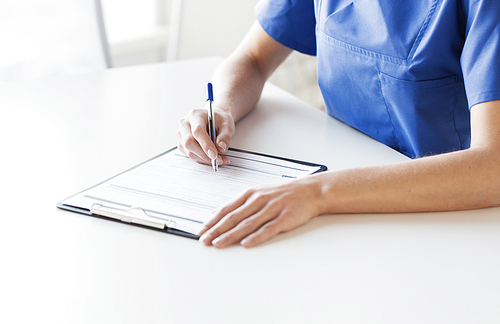 medicine, people and healthcare concept - close up of female doctor or nurse writing medical report to clipboard at hospital
