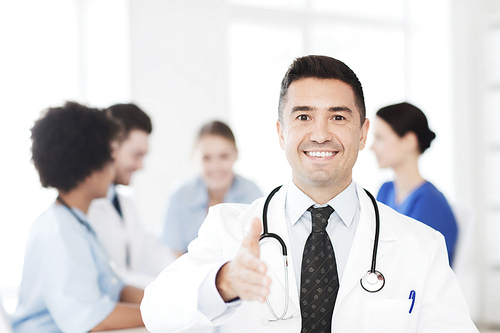 clinic, profession, people and medicine concept - happy male doctor over group of medics meeting at hospital prepared for handshake