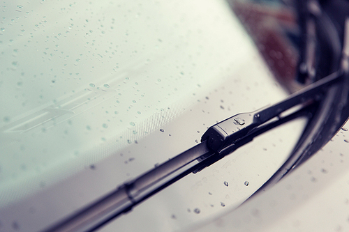 rainy weather and vehicles concept - close up of windshield wiper and wet car glass