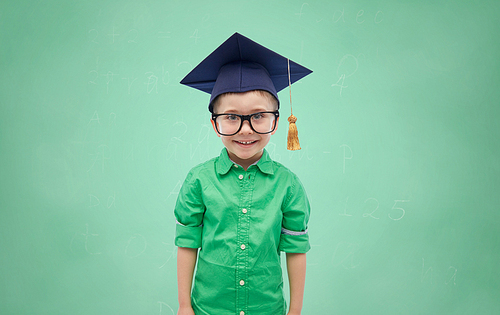 childhood, school, education, learning and people concept - happy boy in bachelor hat or mortarboard over green chalk board background