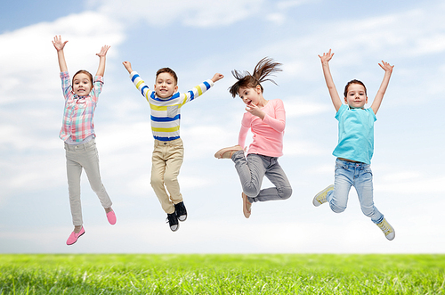 happiness, childhood, freedom, movement and people concept - happy little children jumping in air over blue sky and grass background