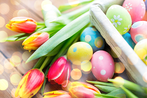 easter, holidays, tradition and object concept - close up of colored easter eggs in basket and tulip flowers over holidays lights